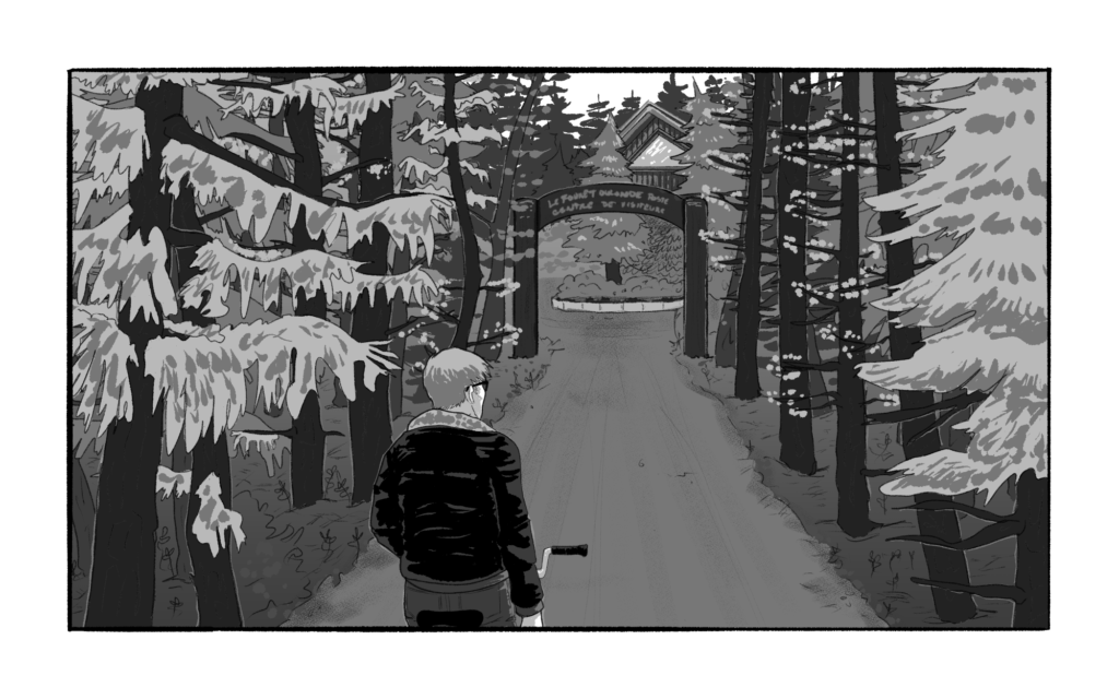 Blythe sits on his bike in the middle of a narrow dirt road surrounded on either side by pine trees. The road passes under an arched wooden sign. The peaked roof of a building peeks out through the trees.